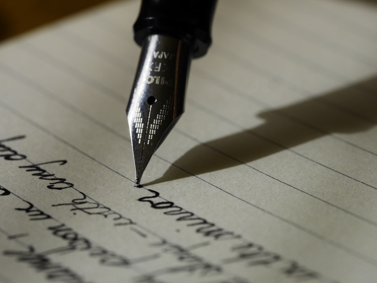 A fountain pen lying on a sheet of black lined paper.