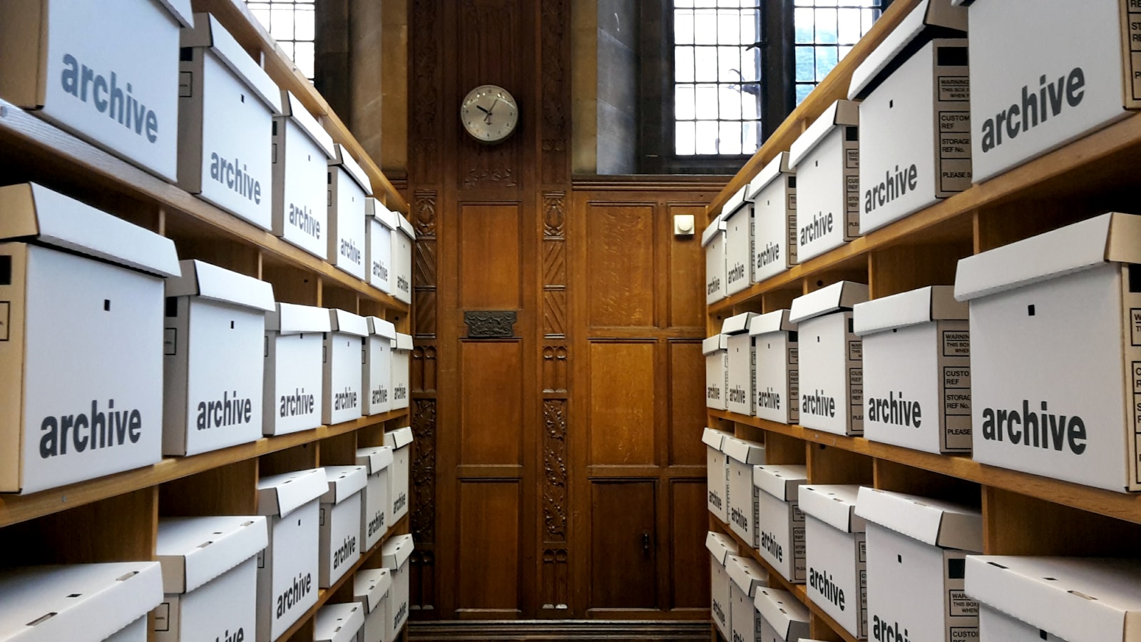 Rows of labelled archive boxes on wooden shelves.